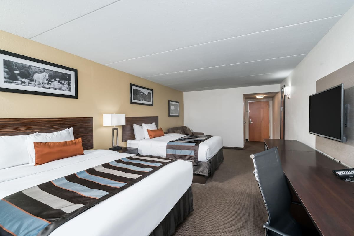 Ein Hotelzimmer mit zwei Betten, einem Schreibtisch, einem Fernseher und gerahmten Bildern an der Wand.