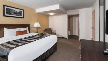 Habitación de hotel con cama, escritorio, silla, lámpara y un cuadro en la pared.