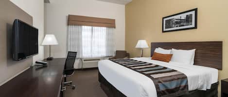Habitación de hotel con cama, escritorio, silla, televisor, lámparas y un cuadro en la pared.