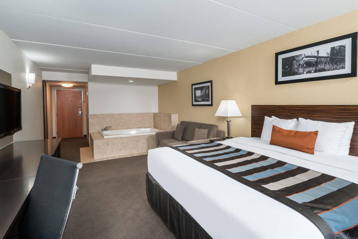 Ein Hotelzimmer mit Bett, Sofa, Schreibtisch, Stuhl, Lampe, einem Bild an der Wand und einer Tür zu einem Badezimmer.