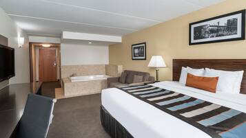 A hotel room with a bed, a sofa, a desk, a chair, a lamp, a picture on the wall, and a door leading to a bathroom.