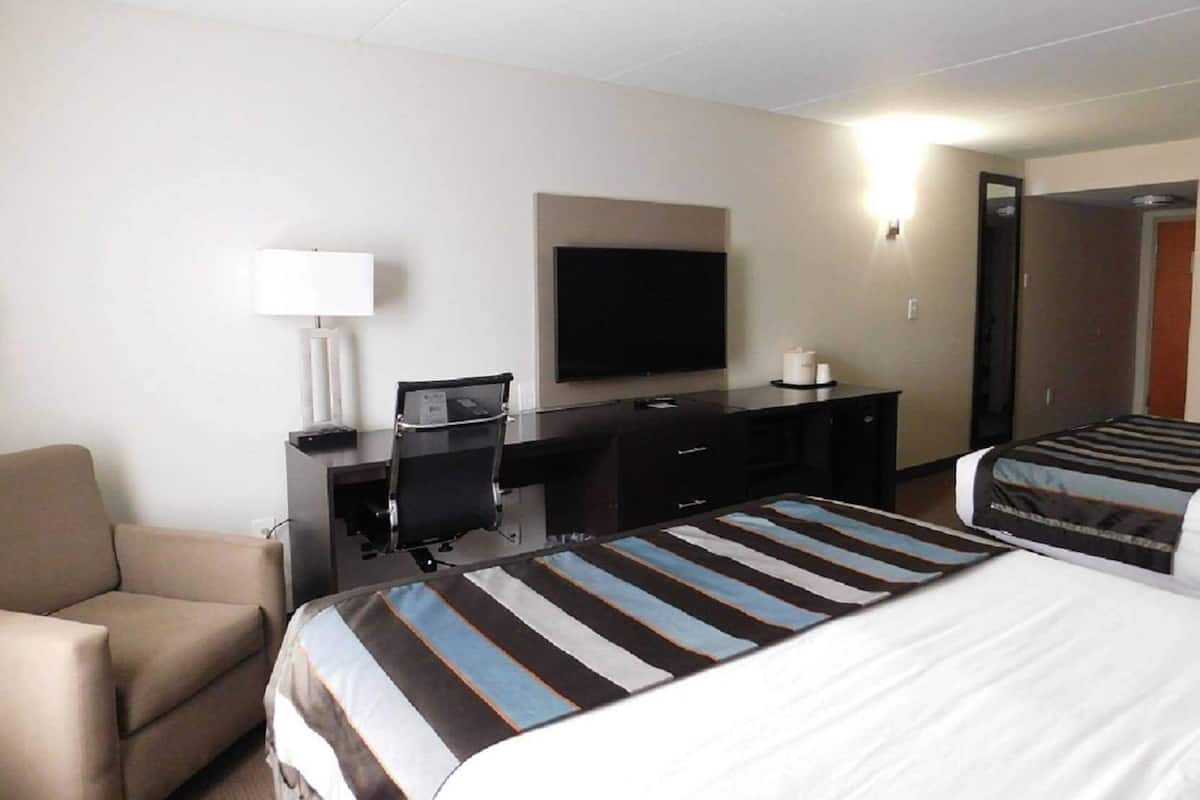 Ein Hotelzimmer mit einem Bett, einem Schreibtisch mit Stuhl, einem Fernseher und einer Lampe.