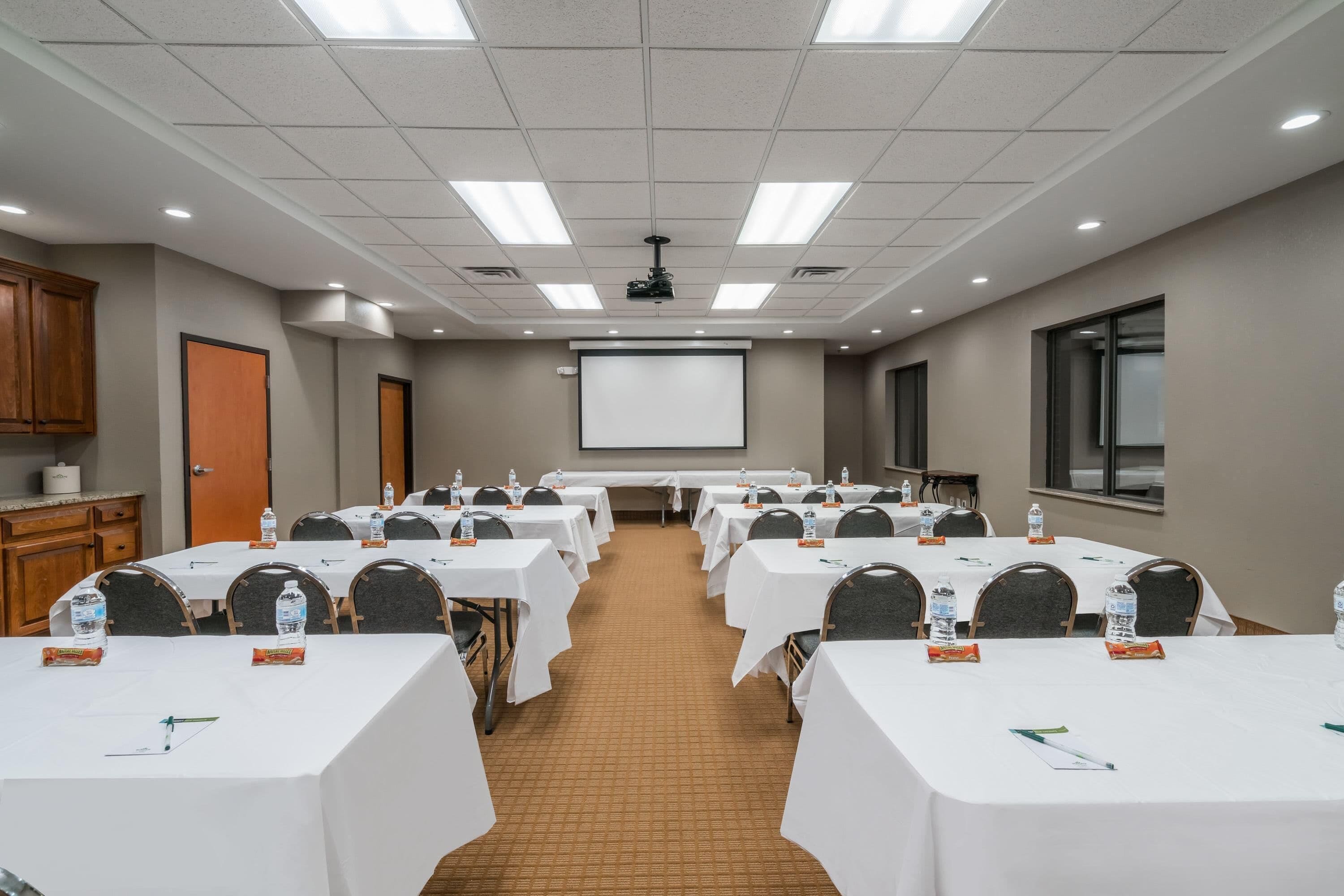 A conference room with multiple tables, chairs, a projector screen, and a presentation screen.