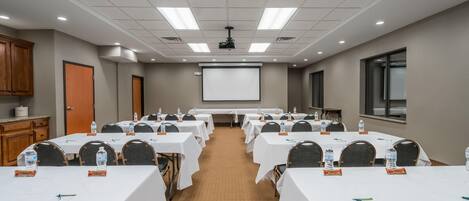 A conference room with multiple tables, chairs, a projector screen, and a presentation screen.