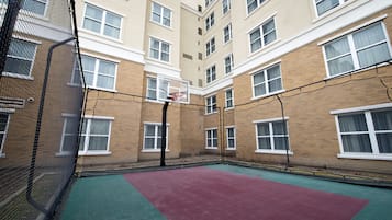 Un terrain de basket intérieur, équipé d’un panier, entouré d’un bâtiment en briques doté de nombreuses fenêtres.
