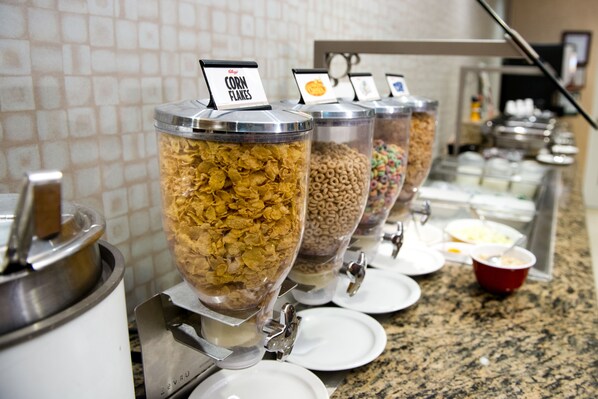 Un bufé de desayuno con recipientes etiquetados de cereales y frijoles.