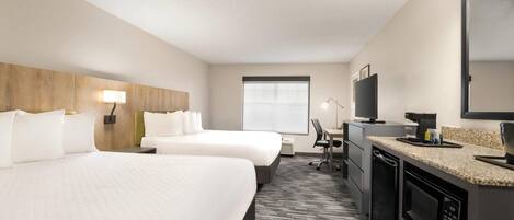 Ein Hotelzimmer mit zwei Betten, einem Schreibtisch, einem Sessel, einem Fernseher, einer Mikrowelle und einem Fenster.