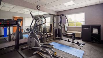 Une salle de sport équipée de machines de cardio, d’appareils de musculation et d’un banc.