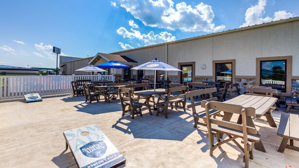 An outdoor patio area with wooden tables and chairs, umbrellas, and a sign for 'SAMUEL ADAMS BOSTON LABER'. - Best Western Nittany Inn Milroy (Reedsville)