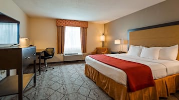 A hotel room with a bed, desk, chair, and a window with curtains.