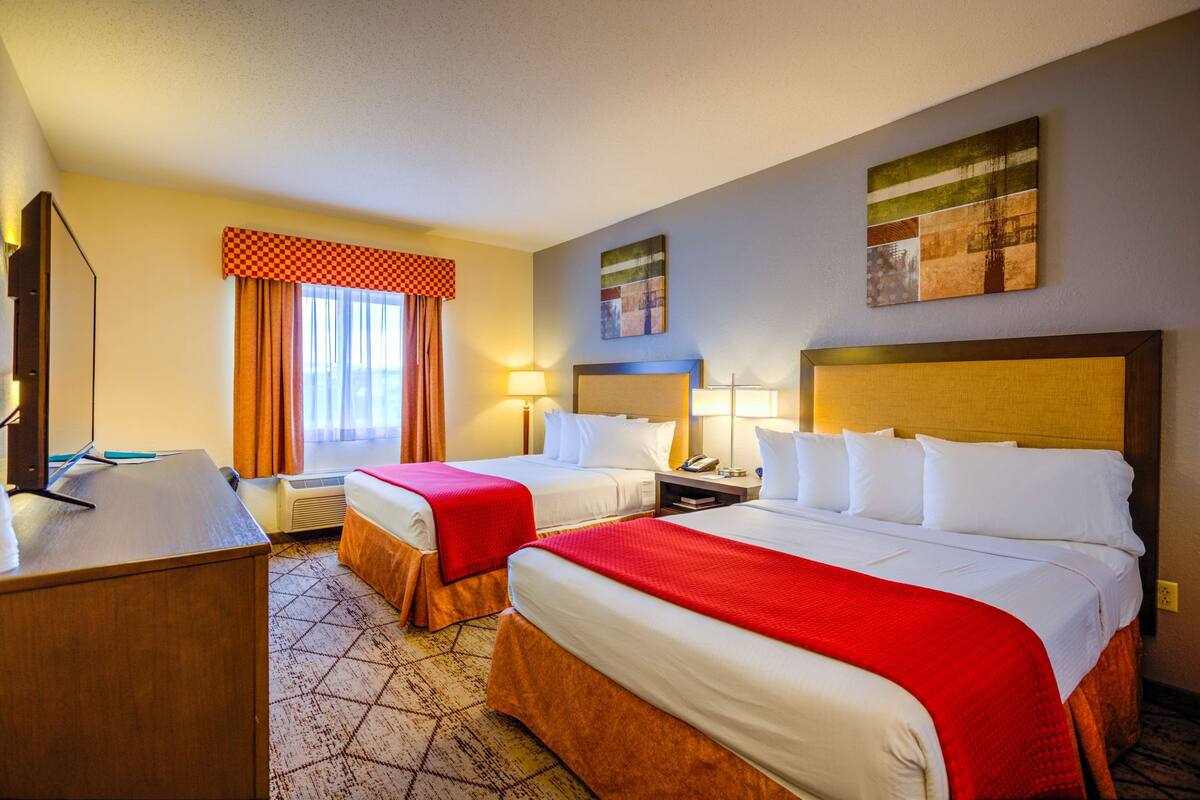 A hotel room with two beds, a desk, a chair, and a window with curtains.