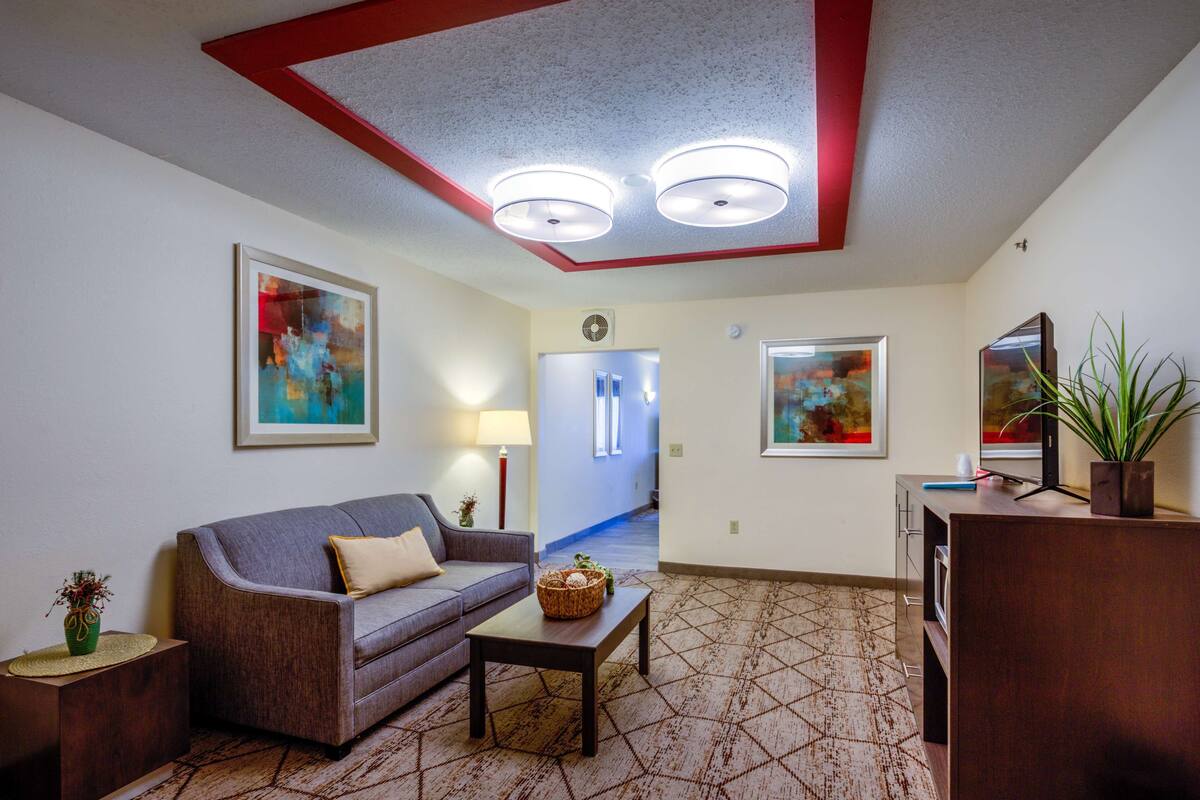 A living room with a sofa, a coffee table, and a TV stand. There are two ceiling lights and a plant on the TV stand.