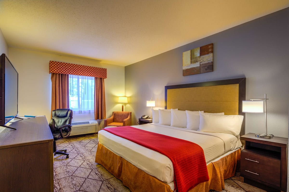 A hotel room with a large bed, a desk, a chair, a lamp, and a painting on the wall.