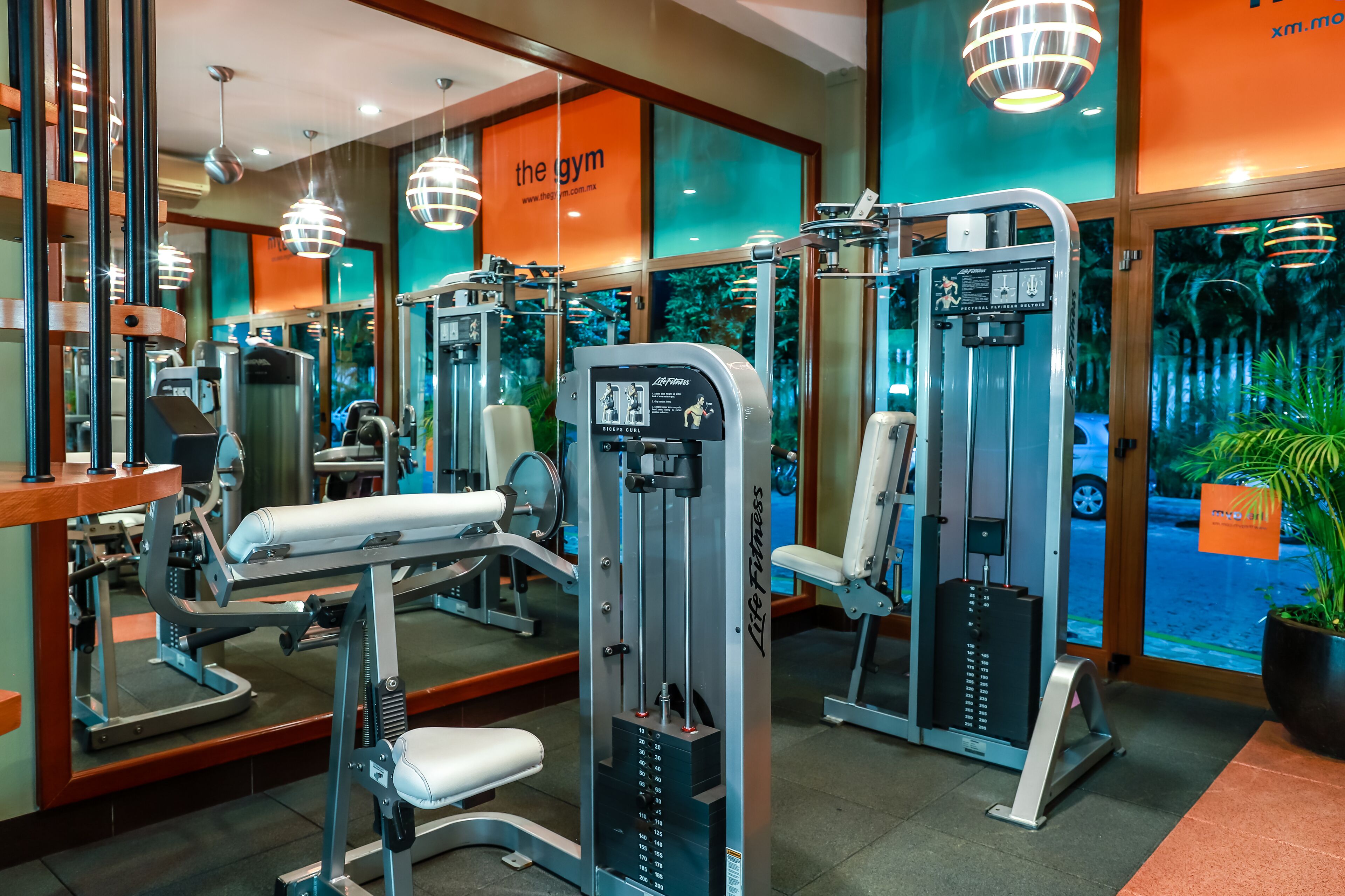 Uma academia com diversos equipamentos de exercício, um espelho grande e vista para o exterior através de amplas janelas.