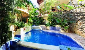 A swimming pool with a small waterfall, surrounded by lush tropical plants and a stone pathway. - Villas Sacbe Condo Hotel and Beach Club (Playa del Carmen)