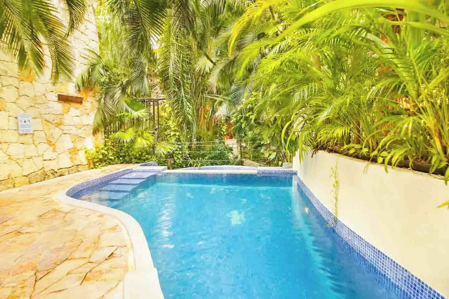 A swimming pool with a tiled edge, surrounded by lush greenery and stone walls.