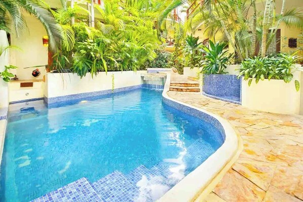 A swimming pool with blue tiles, surrounded by greenery and a tiled deck. - Villas Sacbe Condo Hotel and Beach Club (Playa del Carmen)