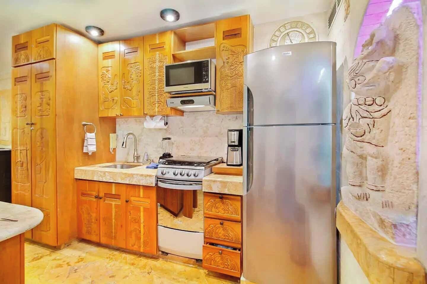 Eine Küche mit Holzschränken, einer Mikrowelle, einem Herd, einem Kühlschrank und einem Spülbecken.