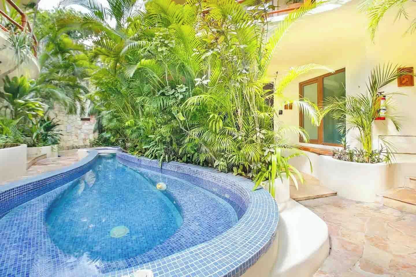 A swimming pool with a tiled edge, surrounded by lush greenery and a stone pathway.