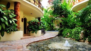 A courtyard with a stone pathway, a small water feature, and lush tropical plants. - Villas Sacbe Condo Hotel and Beach Club (Playa del Carmen)