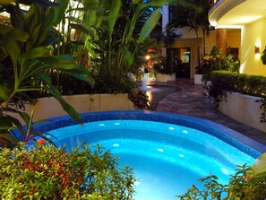 A swimming pool with a tiled edge, surrounded by lush greenery and a stone pathway leading to a building entrance. - Villas Sacbe Condo Hotel and Beach Club (Playa del Carmen)