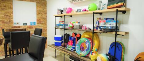 A room with a brick wall, a whiteboard, a wooden shelf with sports equipment, a black chair, and a desk with a computer.