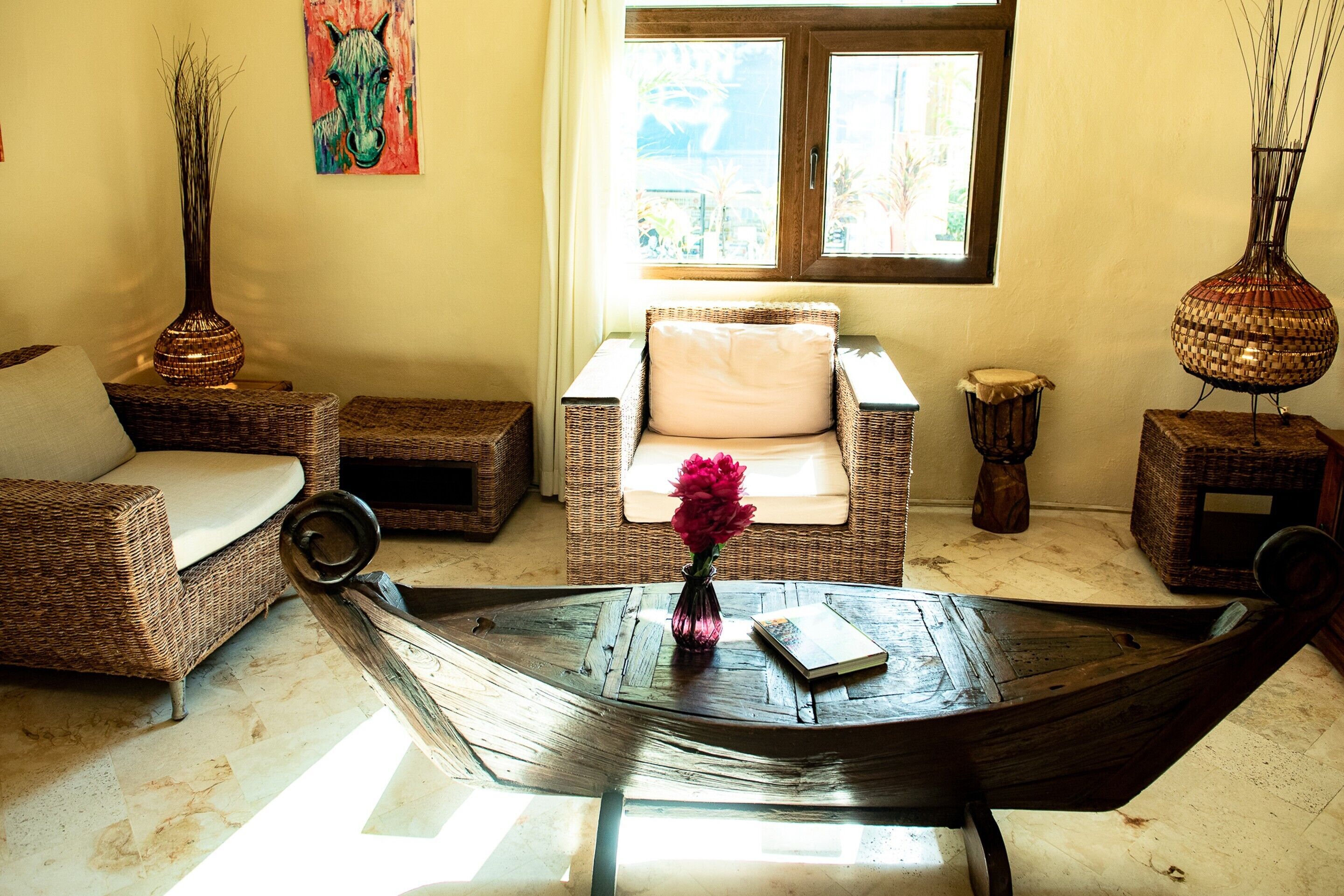 A cozy living area with wicker furniture, a woven coffee table, and a window with a view of greenery.