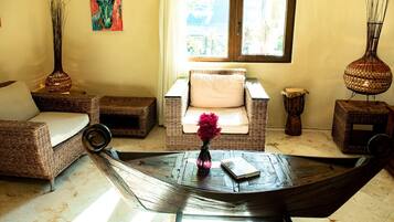 A cozy living area with wicker furniture, a woven coffee table, and a window with a view of greenery.