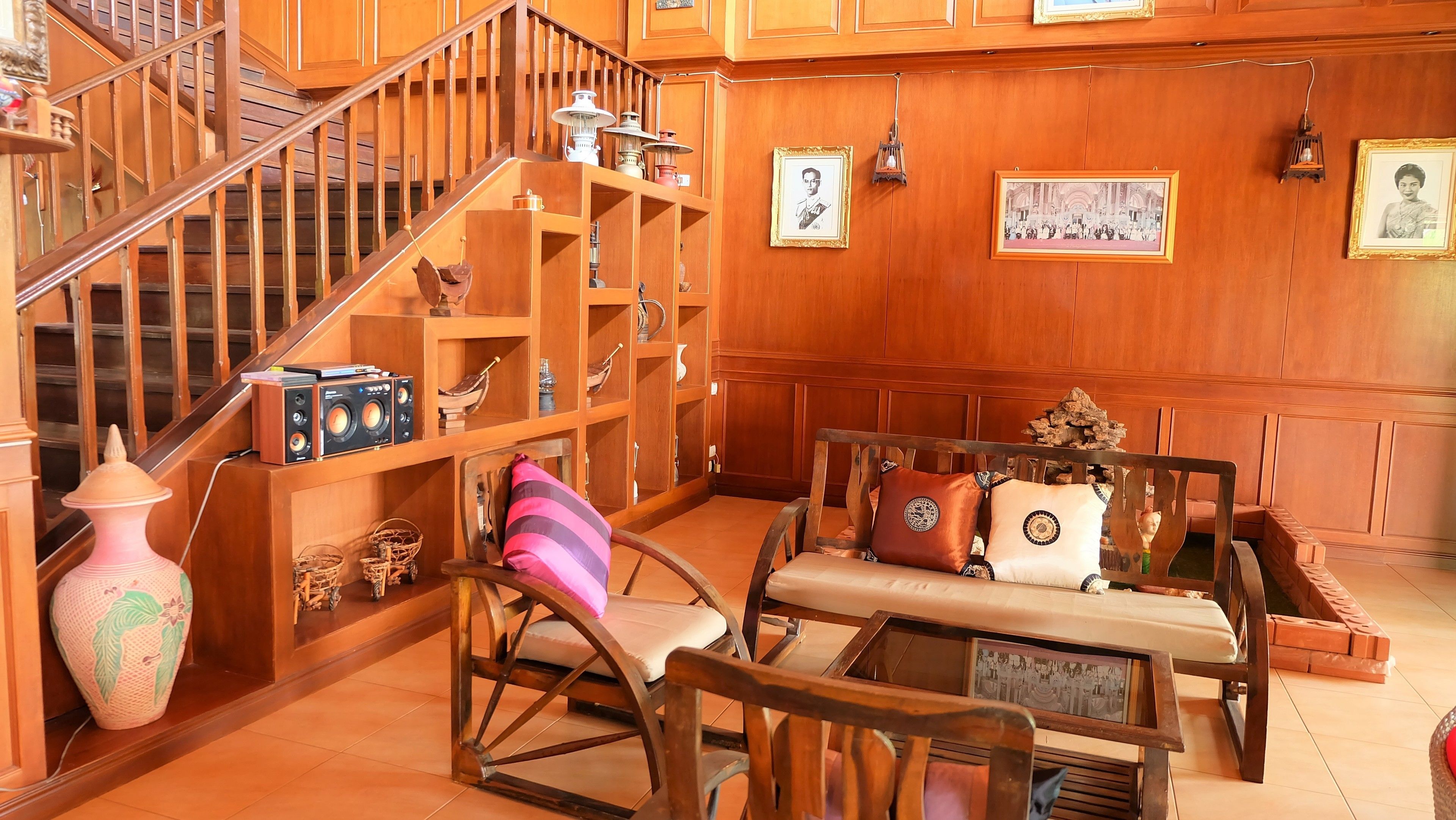 A wooden interior with a staircase, a sofa set, and a collection of framed pictures on the walls.