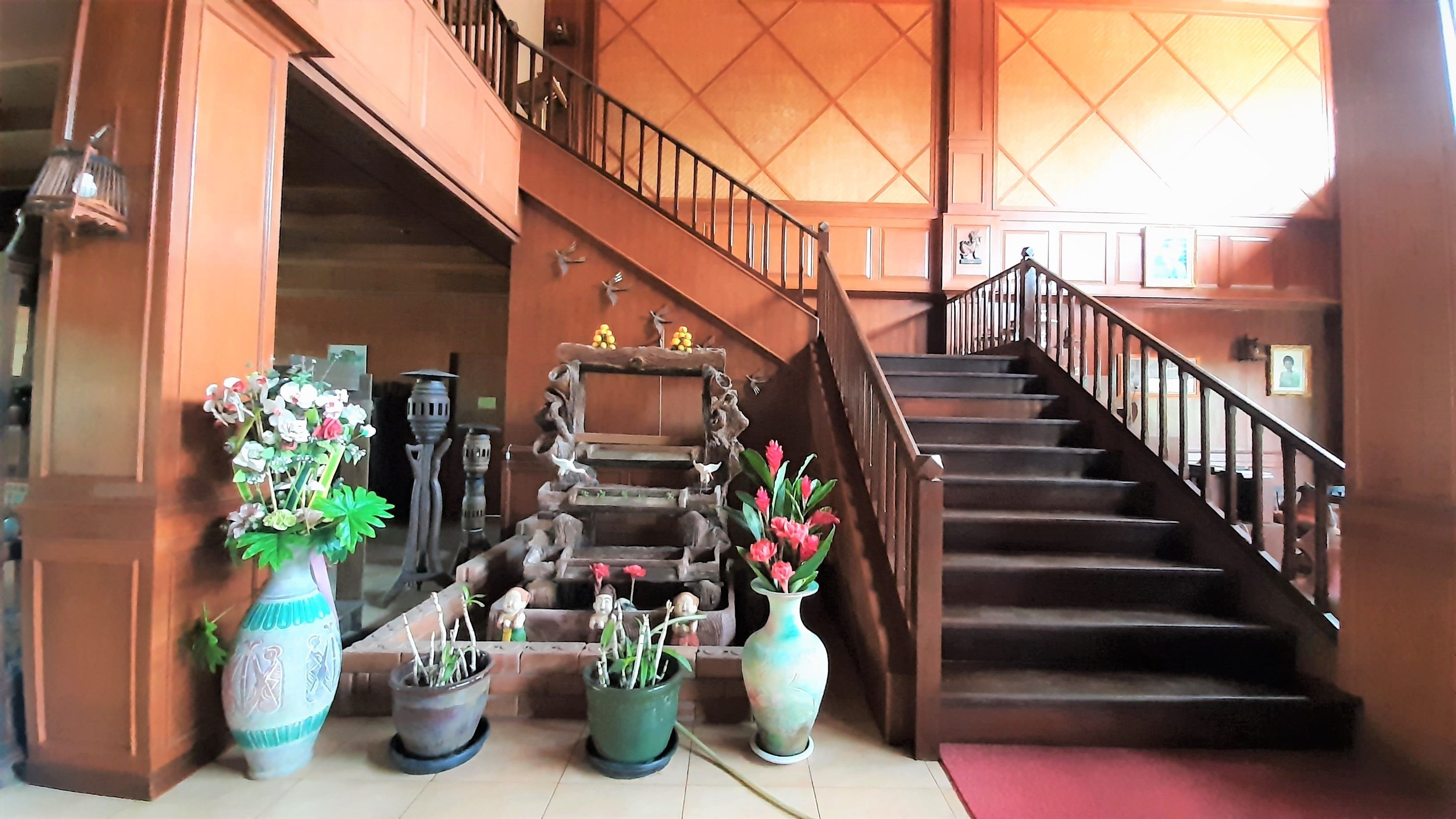A staircase with wooden railings and a red carpet leading to a landing area with potted plants and decorative items.