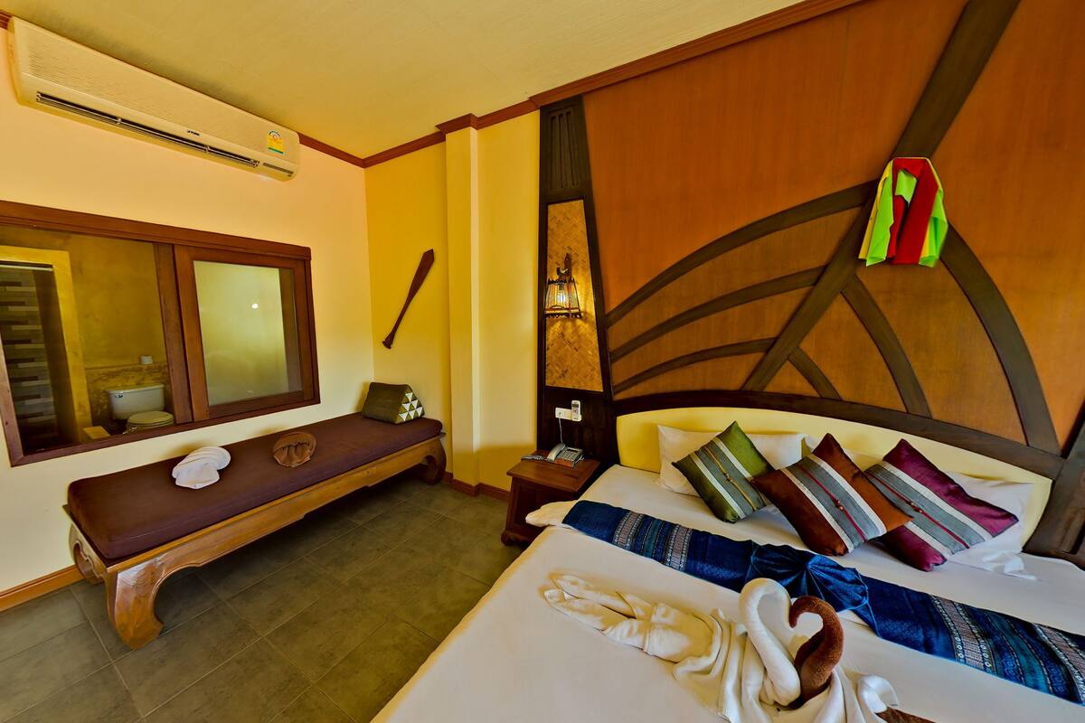 Habitación de hotel con cama, una banca, mesita de noche con teléfono, espejo y unidad de aire acondicionado.