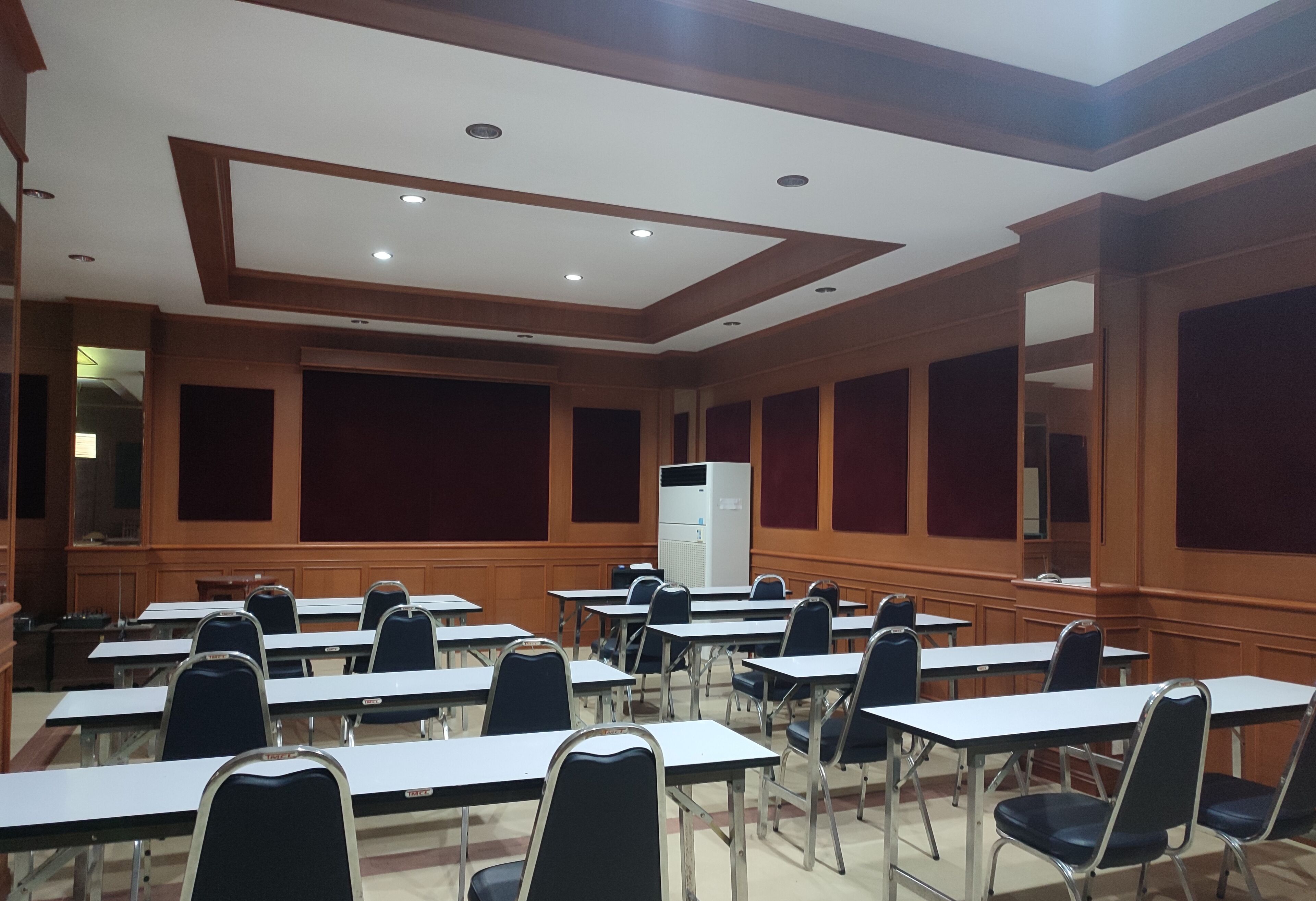 Un salón de conferencias con varias mesas y sillas, paneles de madera e iluminación empotrada.