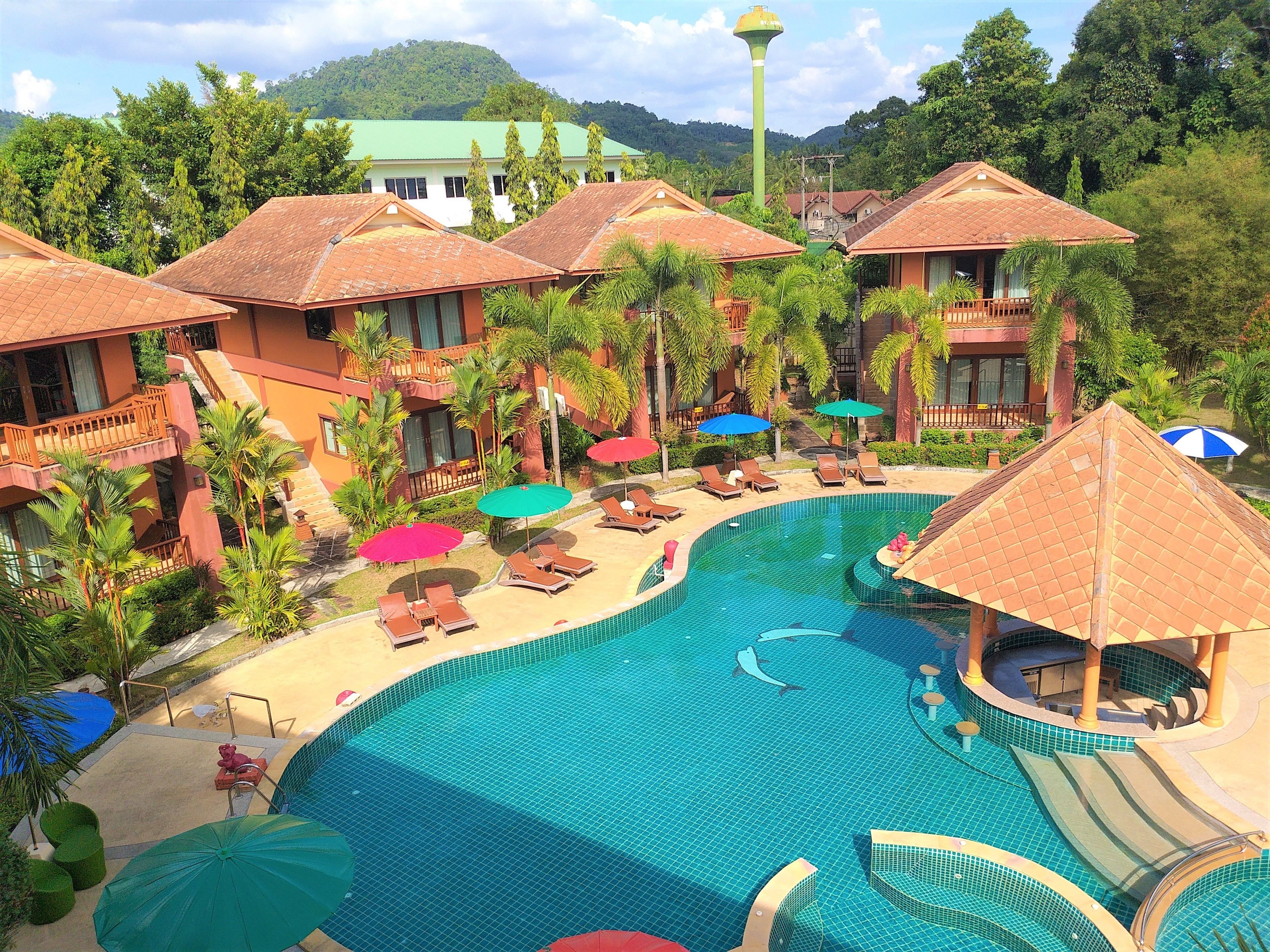 A resort with a large swimming pool, sun loungers, and palm trees.