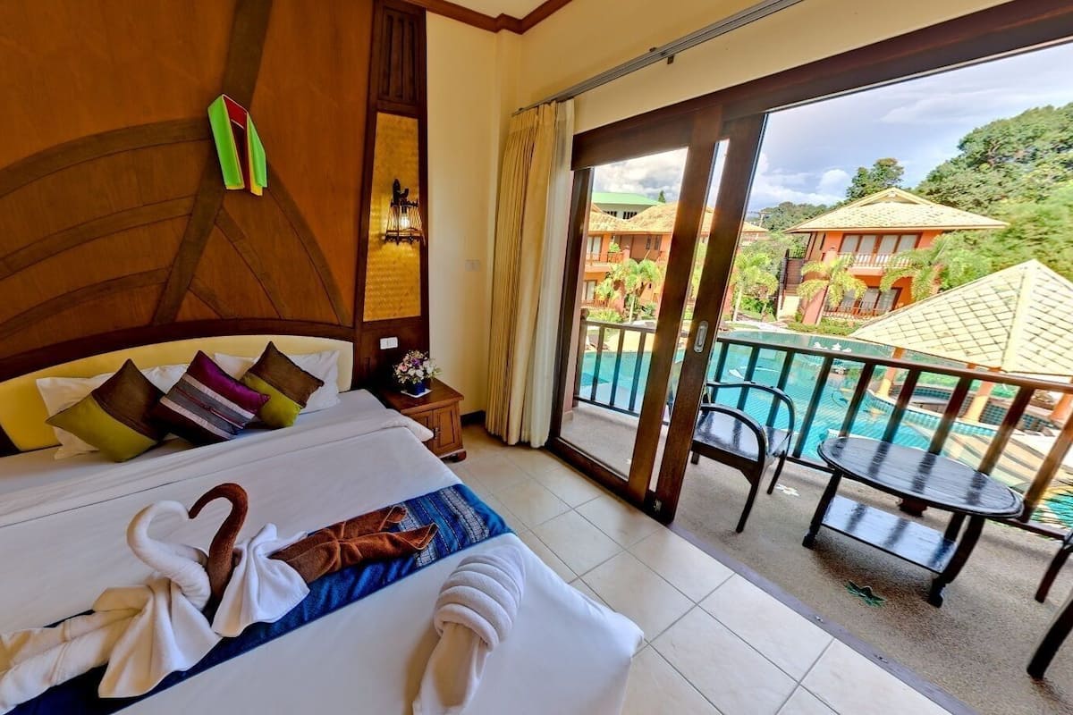 Habitación de hotel con cama, mesita de noche, teléfono y ventana con vistas a una piscina y edificios.