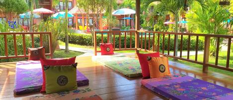 A deck with cushioned seating and a pool in the background.
