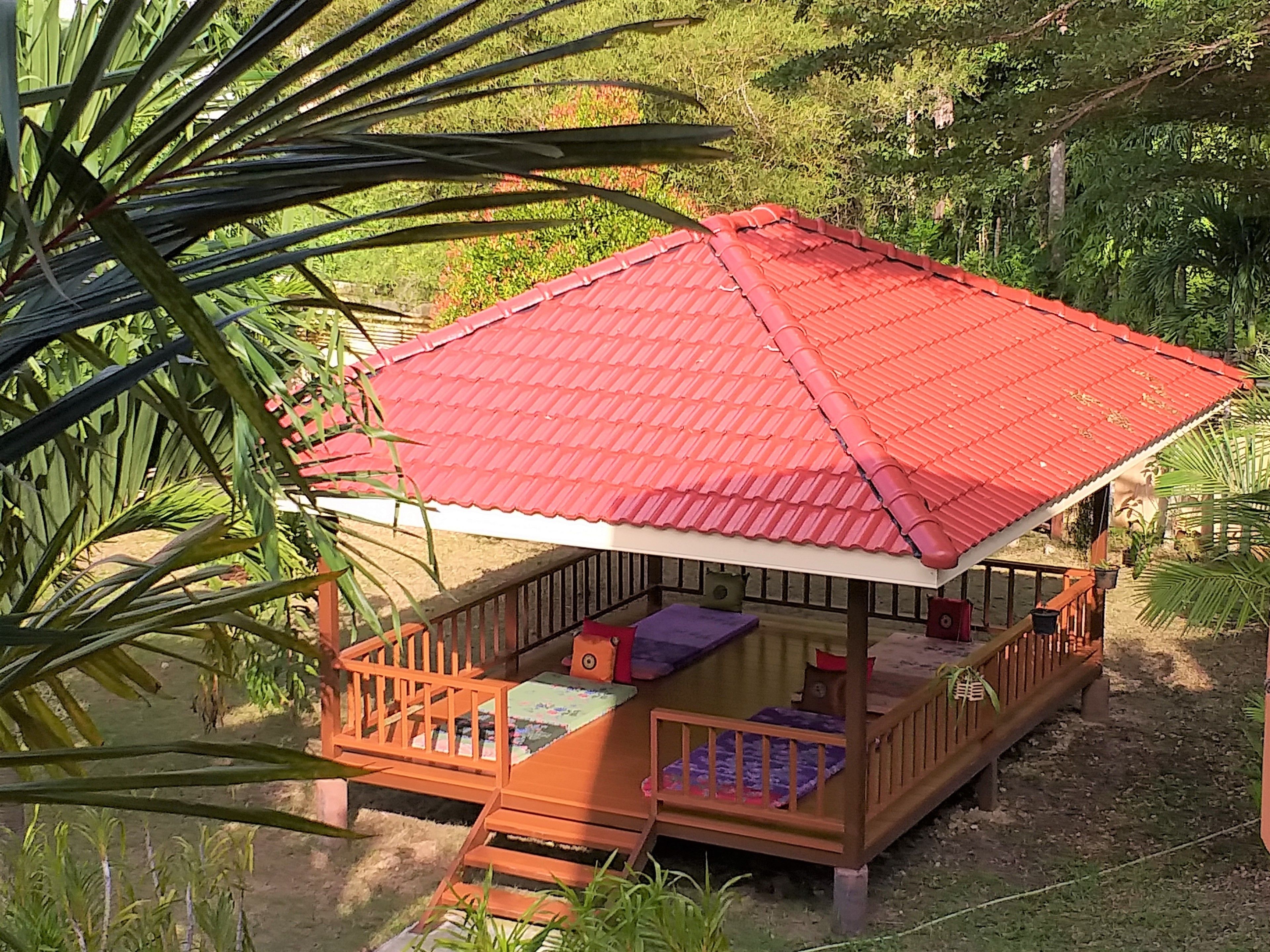 Une structure en bois surmontée d’un toit rouge, entourée de verdure.