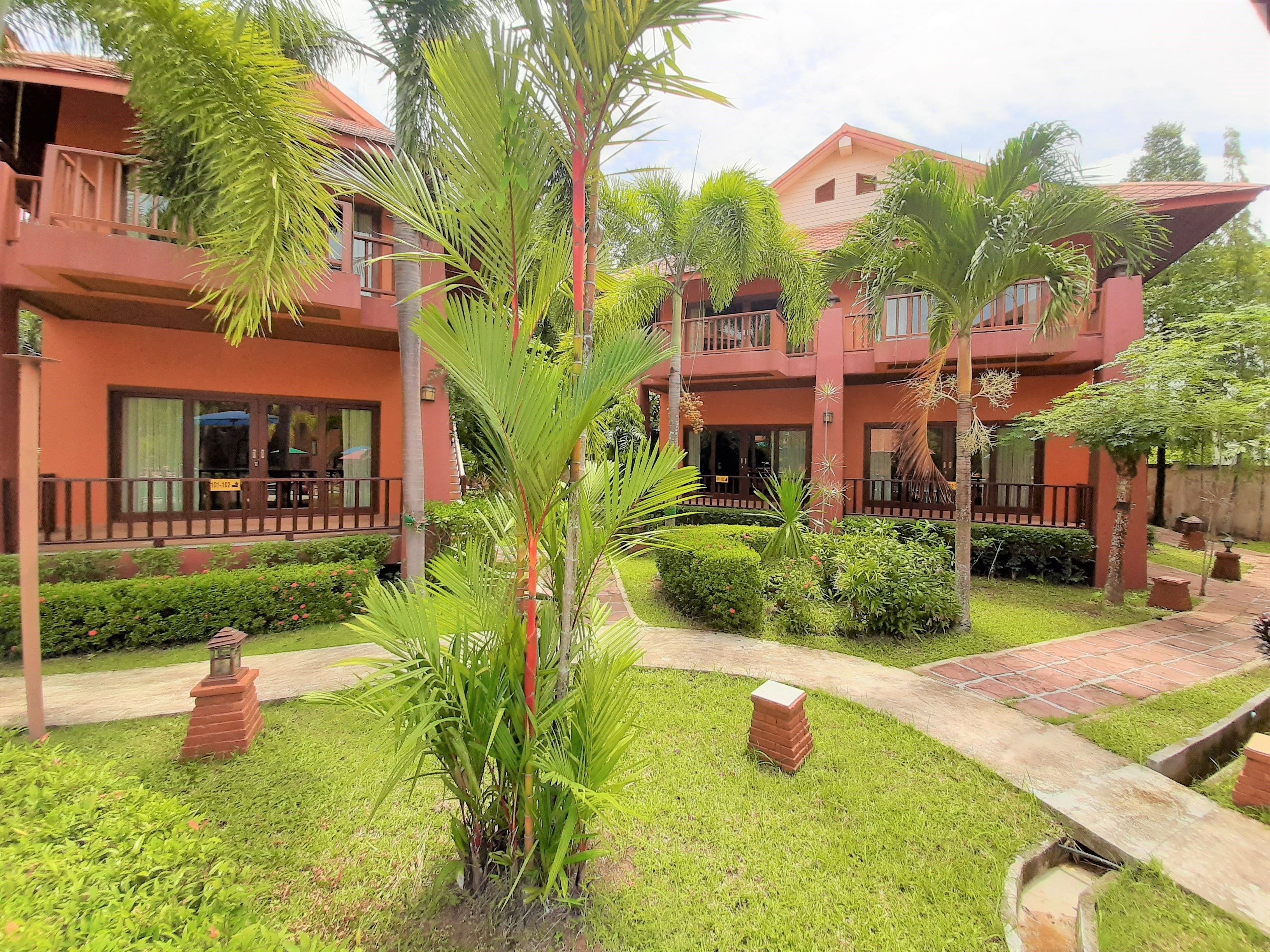 A multi-story hotel with a red facade, a central courtyard with palm trees, and a brick pathway.