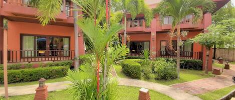 A multi-story hotel with a red facade, a central courtyard with palm trees, and a brick pathway.
