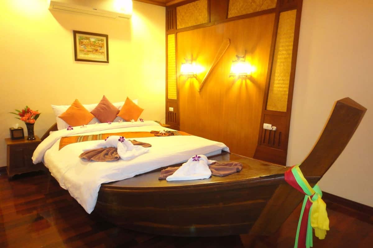 Habitación de hotel con dos camas, cabecero de madera, mesita de noche con un florero y una silla con un lazo de colores.