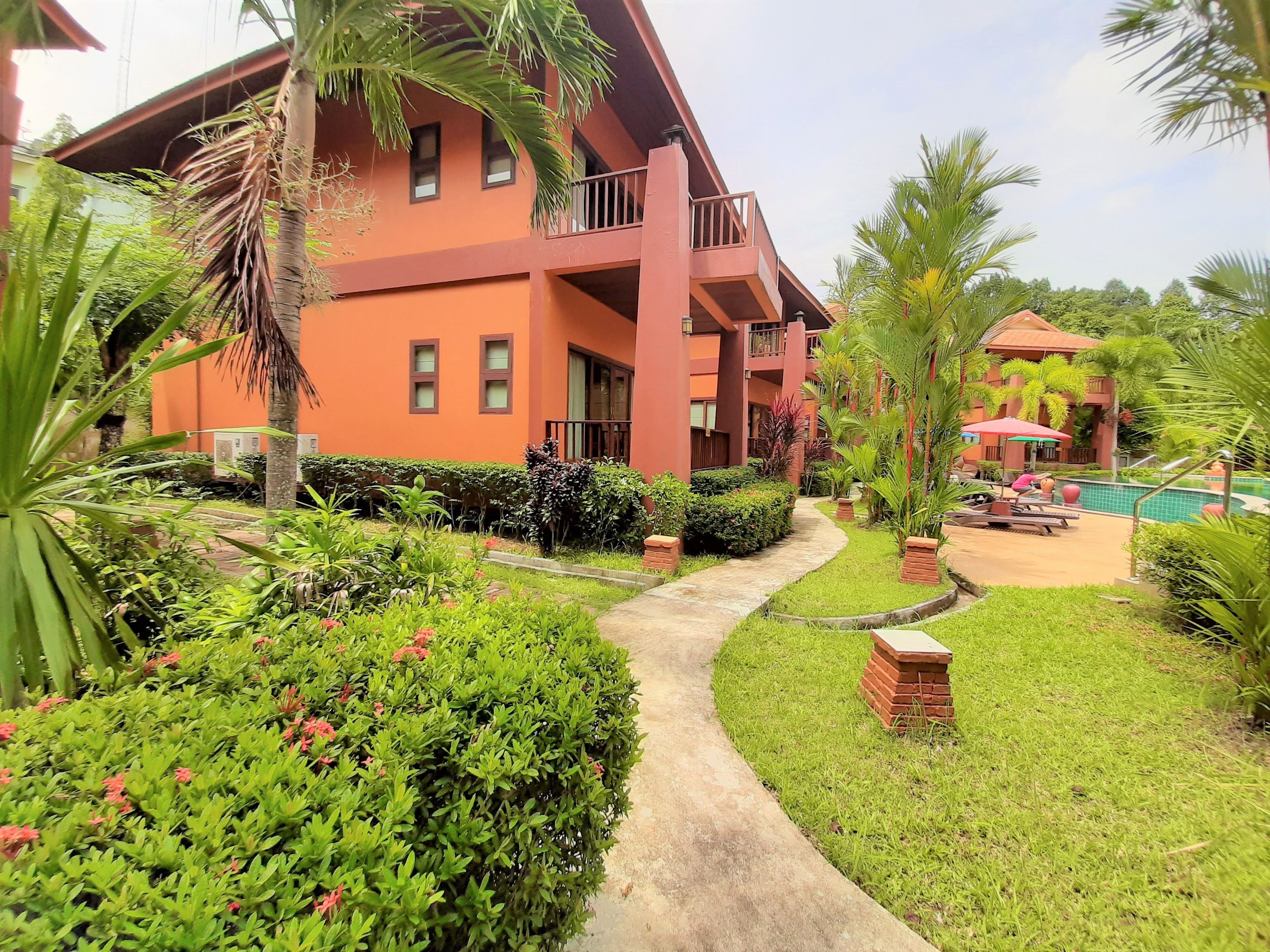 Um hotel com vários andares, fachada vermelha, piscina e vegetação exuberante.