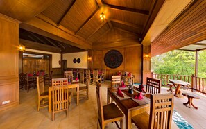 Un restaurant doté de meubles en bois, d’une décoration murale originale et offrant une vue sur la verdure environnante.