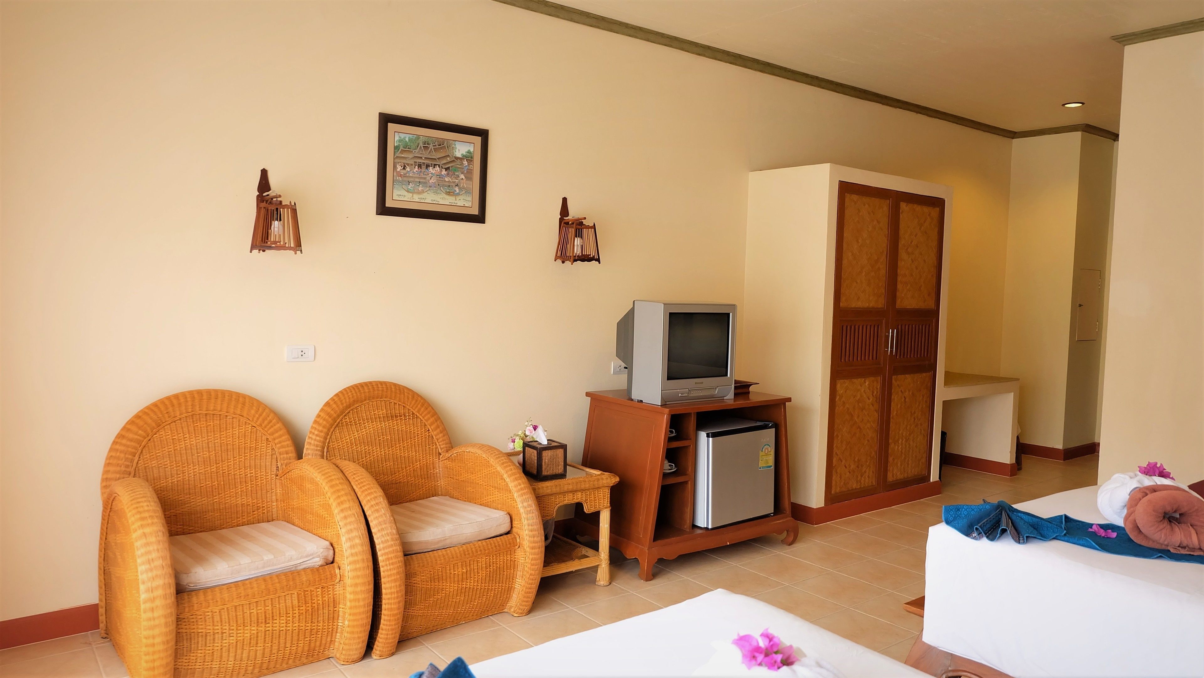A living room with wicker furniture, a television, a small refrigerator, and a wardrobe.