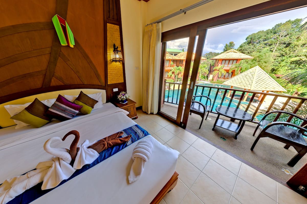 Una habitación de hotel con cama, mesita de noche y ventana con vistas a una piscina y vegetación.