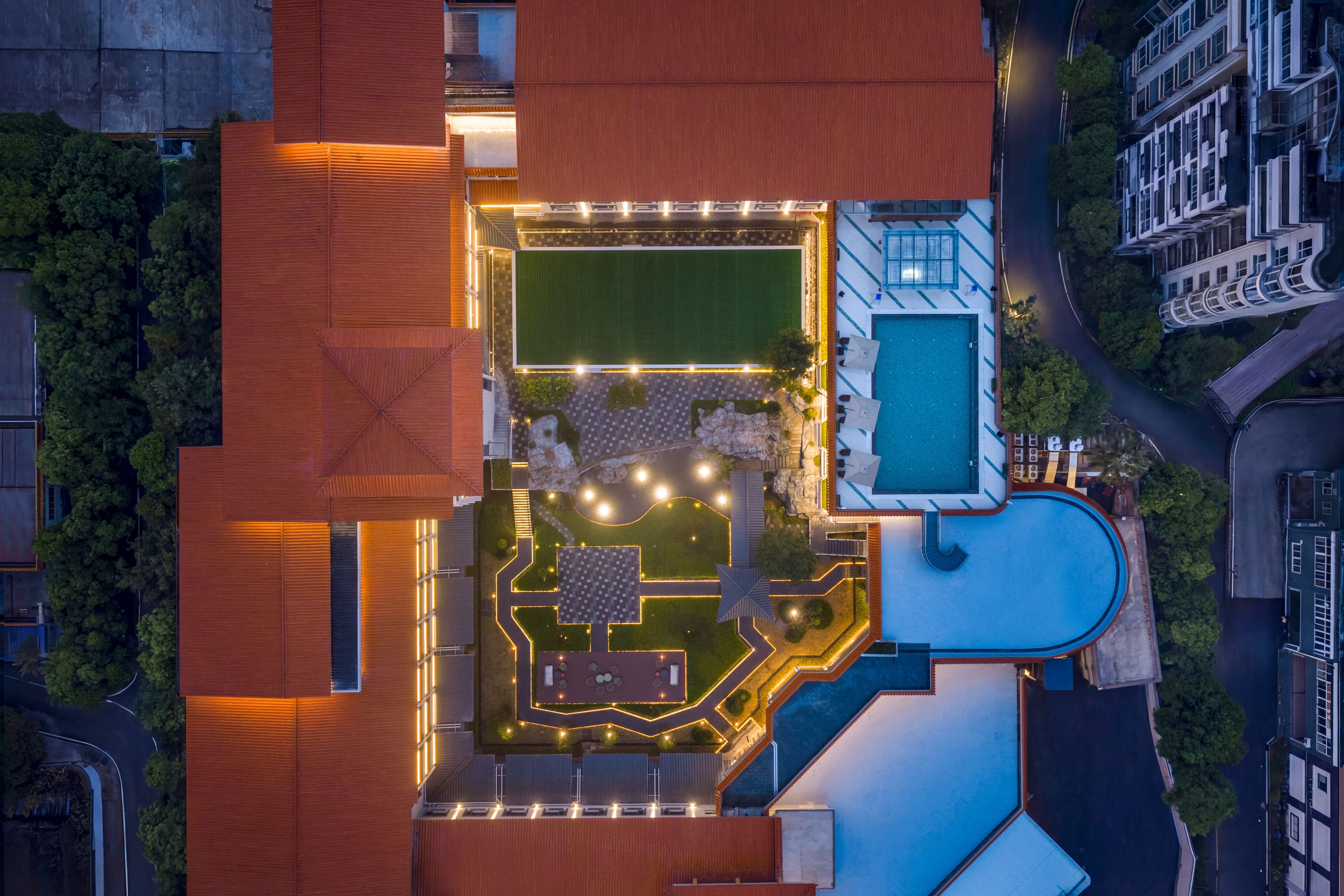 An aerial view of a hotel with a swimming pool, a tennis court, and a landscaped garden area.