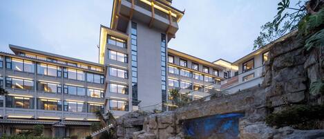 A modern hotel with multiple floors, a stone bridge, and a water feature.