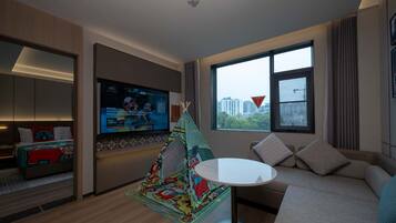 Habitación de hotel moderna con un televisor grande, un sofá acogedor, una pequeña mesa redonda y una colorida tienda de juegos para niños.