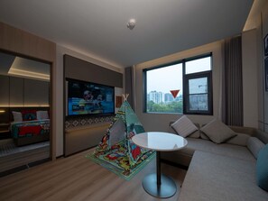 A modern hotel room with a large TV, a cozy sofa, a small round table, and a colorful children's play tent.