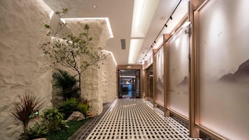 A hallway with a patterned floor, a plant, and a view into another room.