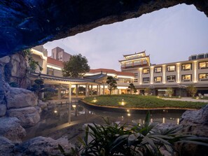 A hotel with a traditional architectural style, a courtyard with a water feature, and a view through a rock archway.