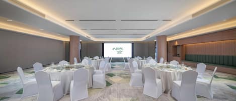 Une salle de conférence avec des chaises et des tables blanches, un écran de projection et un sol recouvert de moquette.